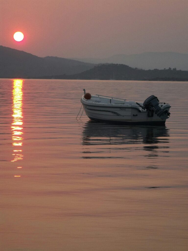 A serene scene of a lone boat on calm waters reflecting the vibrant sunset.