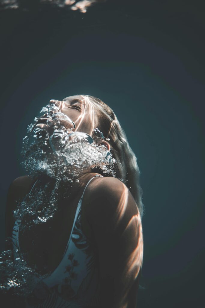 A serene portrait of a woman underwater surrounded by bubbles in a vertical frame.