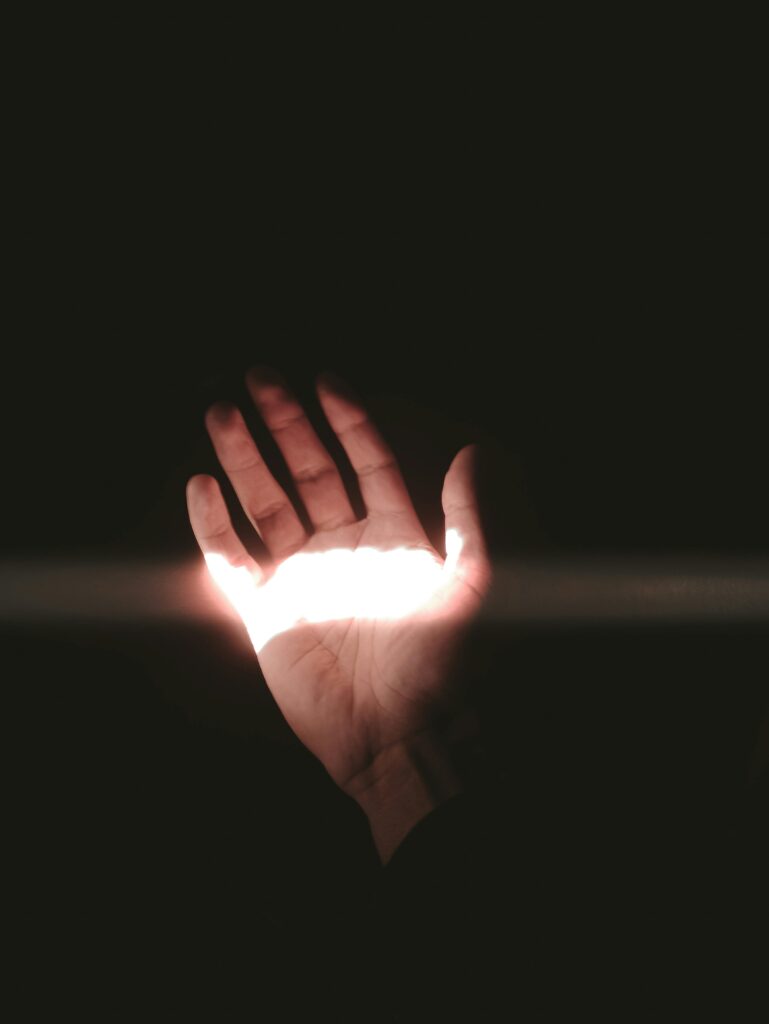 A hand reaching out with light shining through fingers against a dark backdrop.